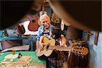 Small family business and traditions: old grandpa with grandson in lute maker shop. The senior artisan gives teaches how to play classic guitar to the boy, who plays his first notes with the instrument