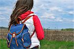 The girl with a backpack standing back and looking at the field