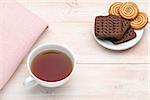 Cup of tea and various cookies on bright wooden background