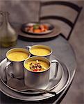 Yellow pepper soup with tomatoes, feta cheese and herb garnish, in metal cups