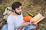 Man in sleeping bag planning with map and smartphone in forest, Deer Park, Cape Town, South Africa