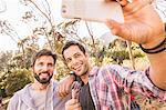 Two men taking smartphone selfie whilst camping in forest, Deer Park, Cape Town, South Africa