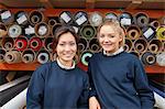 Portrait of two female factory workers in front of textile rolls in roller blind factory