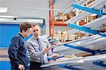 Manager and factory worker checking shelves of metal rods in roller blind factory