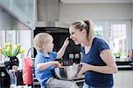 Mother and son fooling around whilst baking, son putting mixture on mother's nose