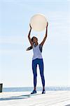 Women wearing sports clothes standing on pier arms raised holding exercise ball