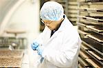 Side view of worker wearing hairnet and latex gloves collecting samples in plastic bag