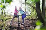 Side view of women in forest face to face holding ankle stretching leg