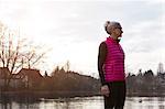 Woman wearing pink bodywarmer in front of pond looking away