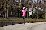 Full length front view of woman nordic walking by pond