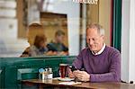 Mature man reading smartphone text at sidewalk cafe table