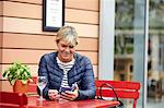 Mature woman reading smartphone texts at sidewalk cafe