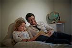 Businessman reading storybook to daughter at bedtime