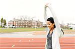 Young woman on running track, stretching