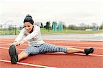 Young woman on running track, exercising, stretching