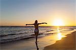 Silhouetted young woman with arms open on beach at sunset, Dominican Republic, The Caribbean