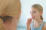 Over the shoulder mirror image of girl applying lipstick