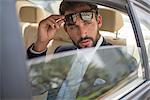 Young businessman holding up sunglasses in car backseat, Dubai, United Arab Emirates