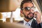 Young businessman wearing sunglasses talking on smartphone in car  backseat, Dubai, United Arab Emirates