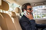 Young businessman in car backseat wearing sunglasses and talking on smartphone, Dubai, United Arab Emirates