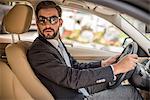 Young businessman driving car looking over his shoulder, Dubai, United Arab Emirates