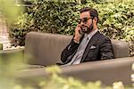 Businessman talking on smartphone on hotel garden sofa, Dubai, United Arab Emirates