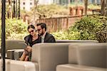 Businessman and woman using digital tablet on hotel garden sofa, Dubai, United Arab Emirates