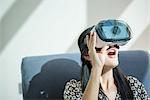 Woman open mouthed on armchair looking through virtual reality headset