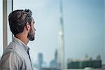 Businessman gazing through window with view of Burj Khalifa, Dubai, United Arab Emirates