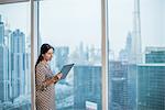 Businesswoman using digital tablet at window, Dubai, United Arab Emirates