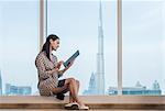 Businesswoman using digital tablet sitting at window, Dubai, United Arab Emirates