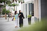 Young middle eastern woman wearing traditional clothing walking along street with female friend, Dubai, United Arab Emirates