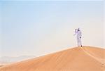 Middle eastern man wearing traditional clothes looking out from desert dune, Dubai, United Arab Emirates