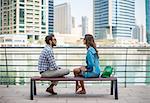 Tourist couple sitting on waterfront talking, Dubai, United Arab Emirates