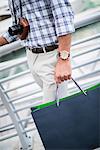 Neck down view of young man strolling on waterfront carrying shopping bag, Dubai, United Arab Emirates