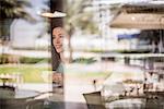 Happy woman behind reflective cafe window, Dubai, United Arab Emirates