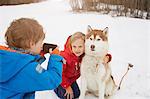 Boy taking smartphone photo of brother and husky in snow, Elmau, Bavaria, Germany
