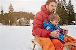 Young man and son tobogganing in snow, Elmau, Bavaria, Germany