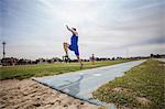 Young male long jumper jumping mid air at sport facility