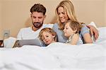 Mother and father in bed with sons looking at digital tablet