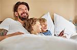 Father and sons in bed using digital tablet laughing