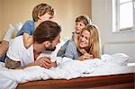 Boys on bed lying on top of parents face to face smiling