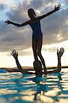 Silhouetted girl balancing on fathers shoulders in swimming pool, Buonconvento, Tuscany, Italy