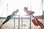 Couple exercising on beach, stretching, using gymnastics parallel bars