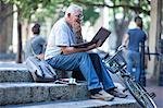 Senior man on city steps using laptop and looking confused