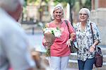 Two mature women carrying bouquet arm in arm in city