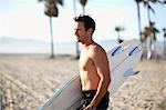 Male surfer carrying surfboard on Venice Beach, California, USA