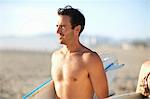 Bare chested male surfer carrying surfboard on Venice Beach, California, USA