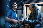 Two musicians in recording studio, singing into microphone and playing guitar