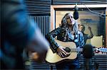 Two musicians in recording studio, singing into microphone and playing guitar